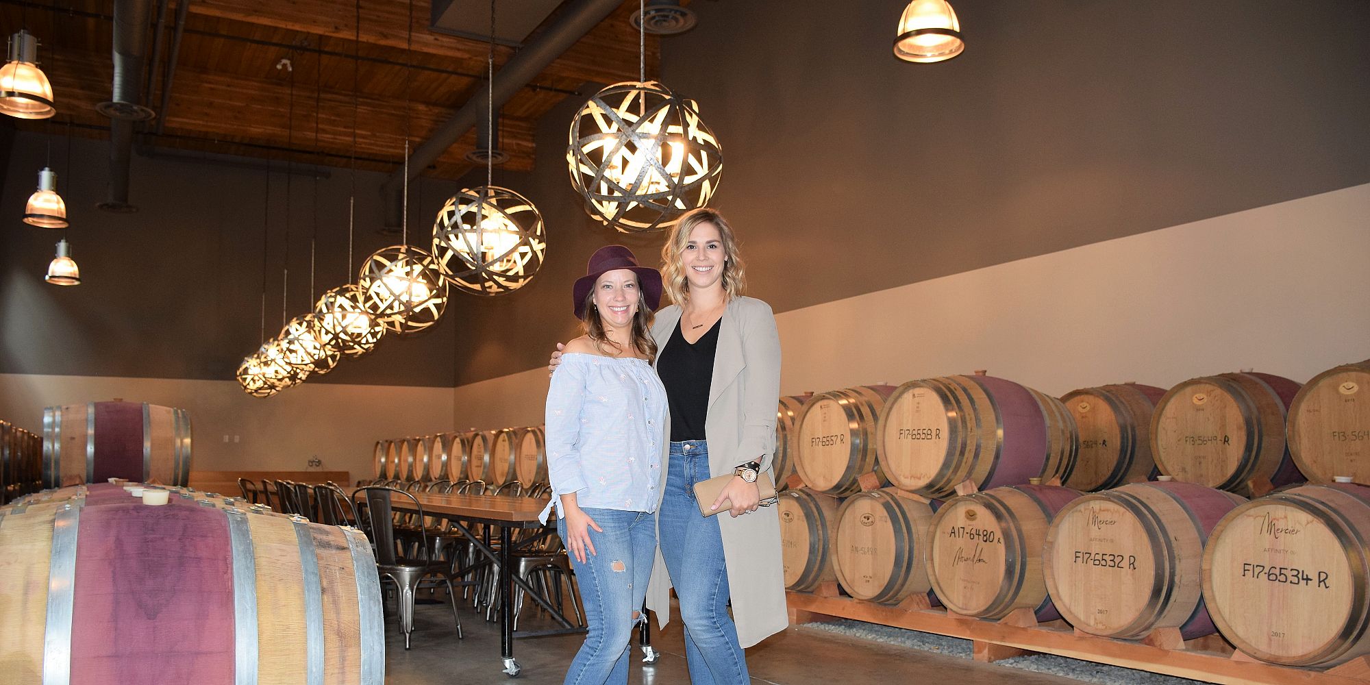 Two Ladies Standing Next To Oak Wine Barrels In The Sandhill Estate Winery Cellar
