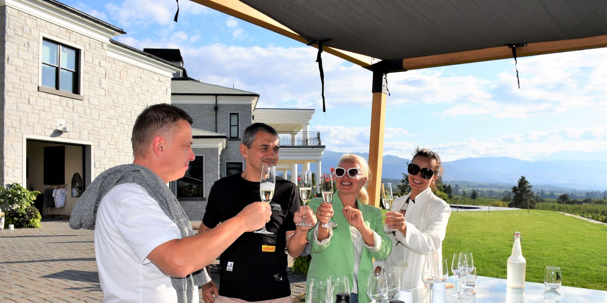 Two Couples Smiling And Cheersing Sparkling Wine At Outdoor Wine Tasting At Kitsch Estate Winery