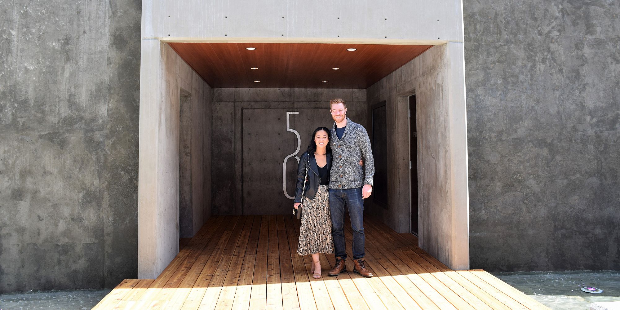 A Couple Standing Next To 50th Parallel Estate Winery's Logo While Dining At The Home Block Resturant