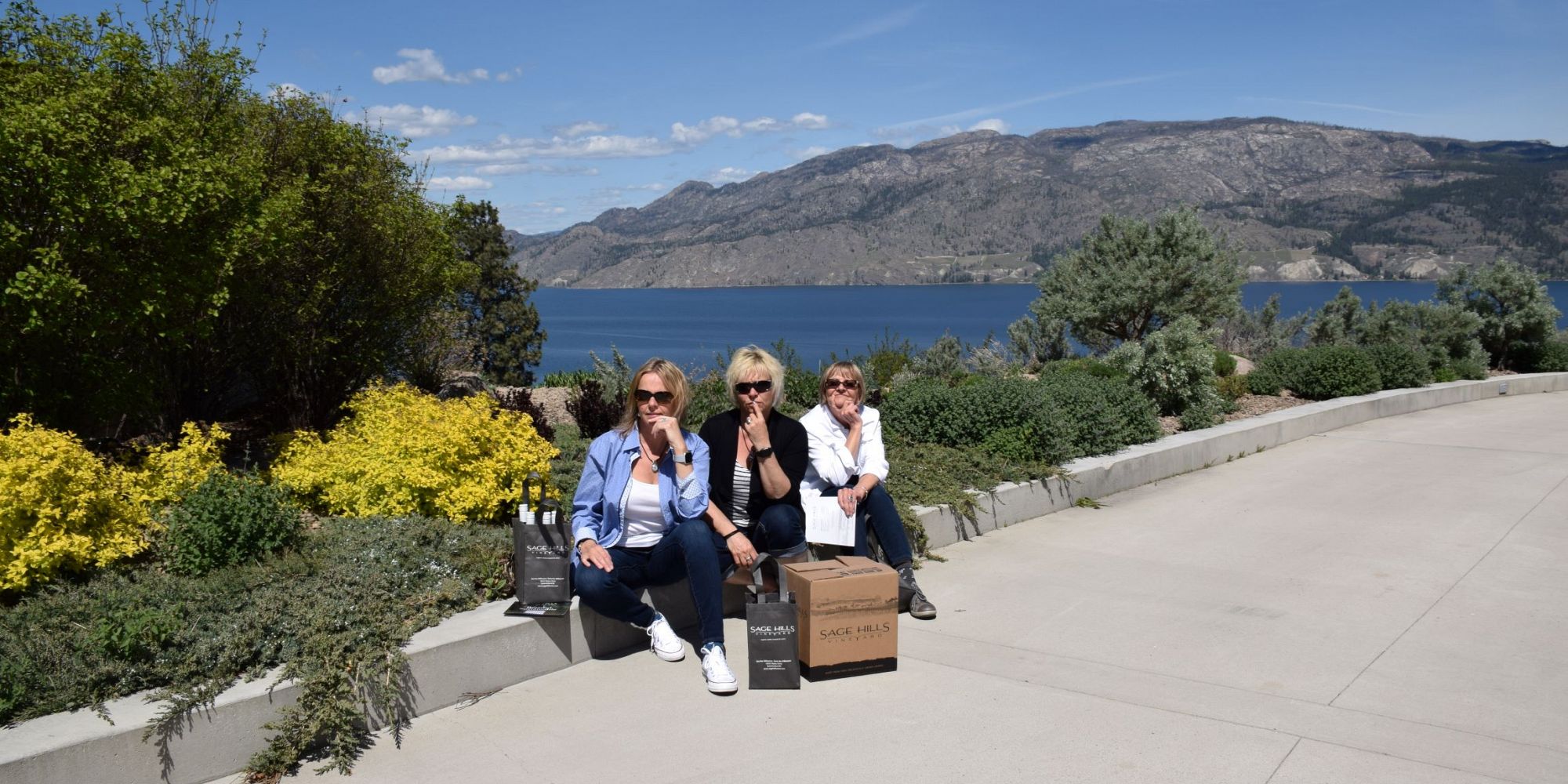 Three Ladies Sitting With Wine Purchased From Sage Hills Estate Winery Overlooking Lake Okanagan
