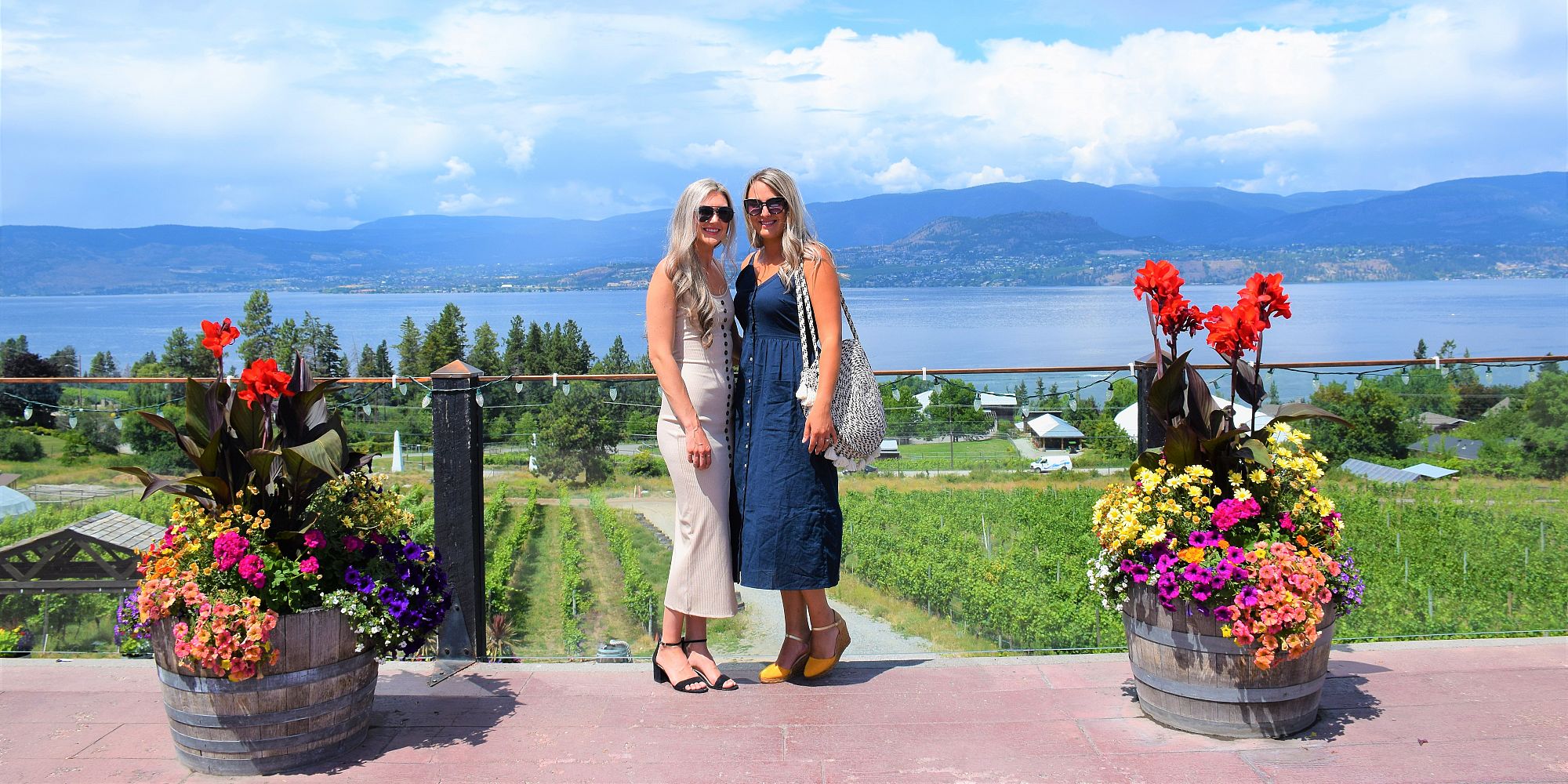 Two Ladies Overlooking Okanagan Lake And A Colorful Flower Garden On The Patio At Summerhill Pyramid Winery