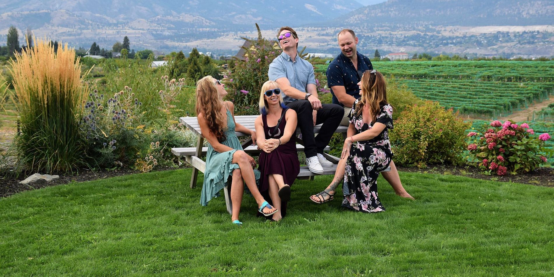 Five Friends Laughing On A Picnic Table Overlooking Vineyards And Okanagan Lake At Da Silva Vineyards
