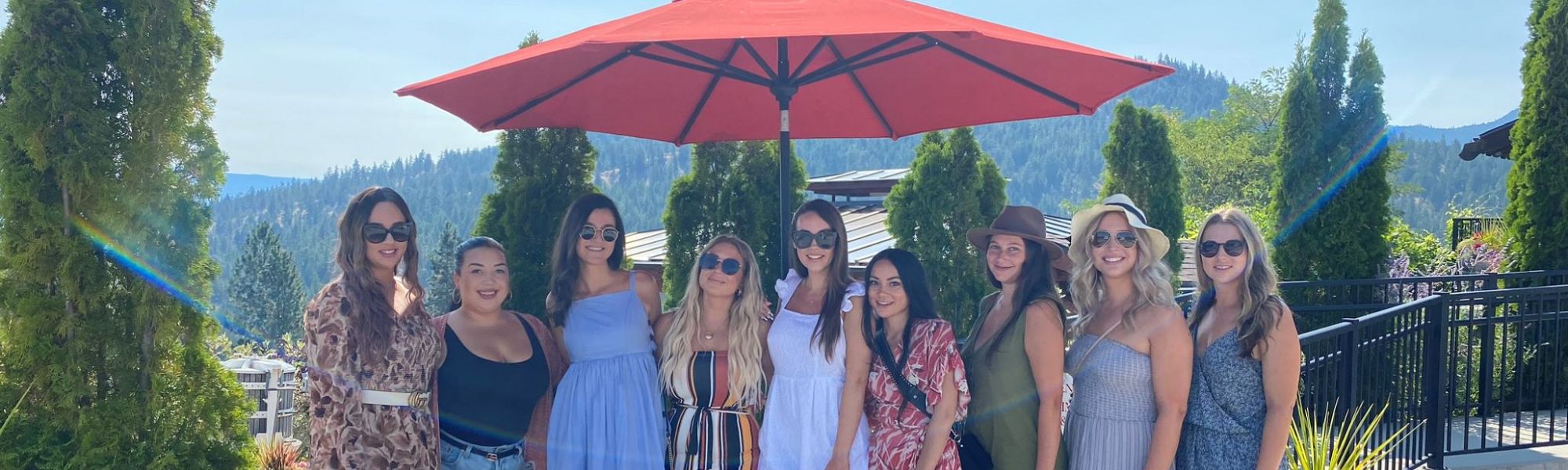 Stagette Party posing on the Dirty Laundry Vineyard patio under a large red umbrella to capture their wine tour experience.