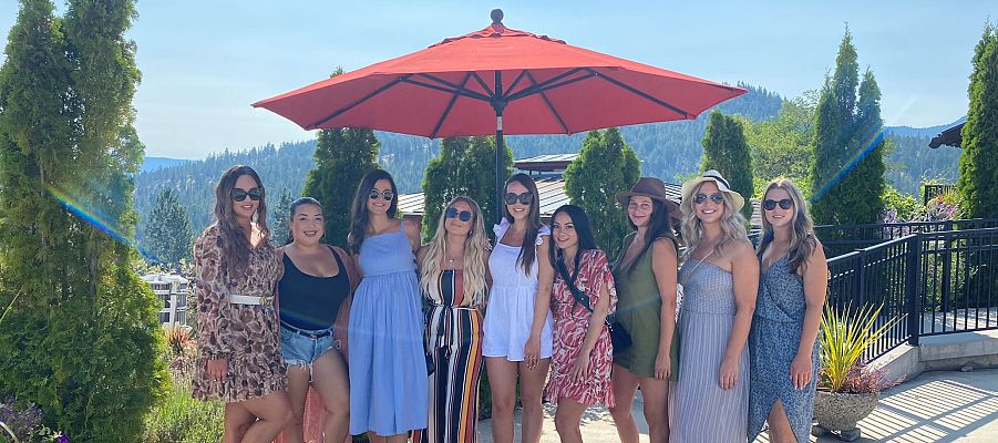 Stagette Party posing on the Dirty Laundry Vineyard patio under a large red umbrella to capture their wine tour experience.